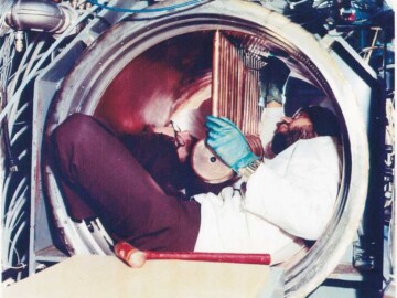 The Alvarez tank. The somewhat cramped quarters of the Alvarez section of the HCTF during installation and alignment of the drift tubes. L-R. J. Ungrin, D. Clements.
<br /><br />
Photo source – AECL. 104-1000