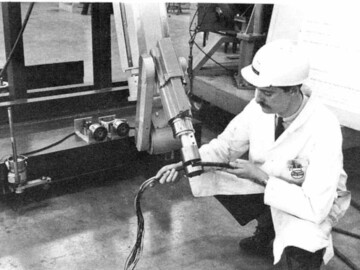 B. Downs shown with a 900-pound pressure shear tool he developed for a remotely controlled robot to carry out repairs in areas not normally open to workers when a reactor is in operation.<br /><br />Photo and caption source – AECL Review, May 1967. 113-1000