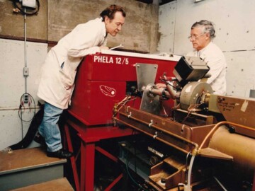 The Pulsed High Energy Linear Accelerator (PHELA). Initially this accelerator, which was located in Bldg. 610 at CRNL and operated with energies up to 12 MeV and 5 kW of beam power, was used to service a number of commercial contracts. These included experiments on behalf of the Department of National Defence, where pulsed-radiation effects on electronic components were examined, and the irradiation of natural topaz to generate colour centers and produce “blue” topaz which is used extensively in the jewellery market. It was later put to use to support CANDU development.In a CANDU reactor every atom in a fuel channel undergoes a number of displacements from the lattice via collisions with neutrons during its lifetime. These displacements lead to changes in the microscopic structure of the fuel channels and to their mechanical properties including, in particular, corrosion resistance. Because charged-particle accelerator beams can be magnetically focussed to very small areas, they can provide particle fluxes orders of magnitude greater than the neutron flux in a reactor. Calculations indicated that even a modest power electron accelerator such as PHELA could be used to produce the annual atomic-displacement levels (typically 1.0 displacement per annum) in pressure-tube samples in a relatively short time (typically 300-400h). Irradiations with PHELA of both Zircaloy and Zr-2.5Nb samples were begun in 1993 and two, several-hundred-hour long irradiations were carried out. In these experiments the temperatures of the samples were maintained to simulate the CANDU operating temperature of 300 degrees C.<br /><br />In the final set of irradiations done with PHELA , the accelerator beam was used to do short-pulse, transient heating of reactor fuel samples (both fresh and irradiated) to allow the measurement of the thermal diffusivity of fuel at high temperatures as a function of burn-up. Making adjustments on the beamline shown in the photo are A. Davidson and I. McIntyre. Photo source-AECL.<br /><br />All industrial accelerator programs ay CRNL were terminated with the closure of the Accelerator Physics Branch on 30 June 1996 due to financial constraints placed on AECL. 124-1000